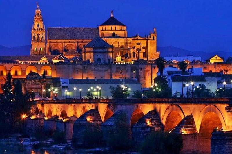La Mezquita-Catedral iluminada de noche junto al Puente Romano de Córdoba